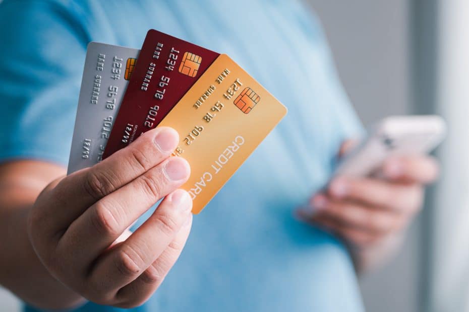 Pessoa segurando três cartões na mão enquanto usa o celular, representando opções de cartão de crédito para negativados e soluções financeiras acessíveis