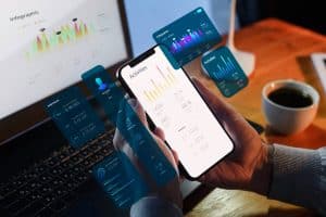Pessoa utilizando smartphone com gráficos financeiros e dashboards digitais, representando o uso de aplicativos para organizar finanças, controle de gastos e análise da vida financeira em tempo real.