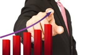 Homem de terno aponta para um gráfico de barras vermelhas em crescimento com uma seta roxa ascendente, representando o aumento dos rendimentos e oportunidades em tempos de juros altos como investir com segurança.