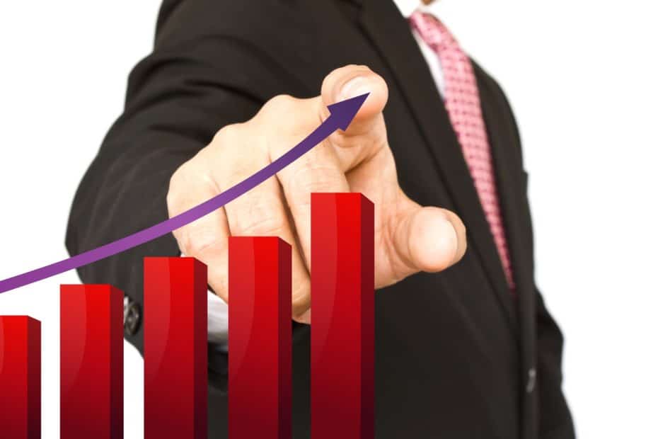 Homem de terno aponta para um gráfico de barras vermelhas em crescimento com uma seta roxa ascendente, representando o aumento dos rendimentos e oportunidades em tempos de juros altos como investir com segurança.