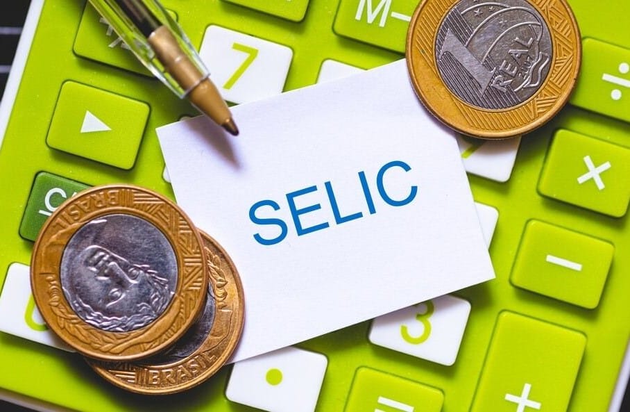 Calculadora verde com moedas de um real e um papel escrito “SELIC”, representando o cálculo de rendimentos e a importância de escolher investimentos seguros, como CDBs e Tesouro Selic, para aplicar a reserva de emergência quanto guardar.
