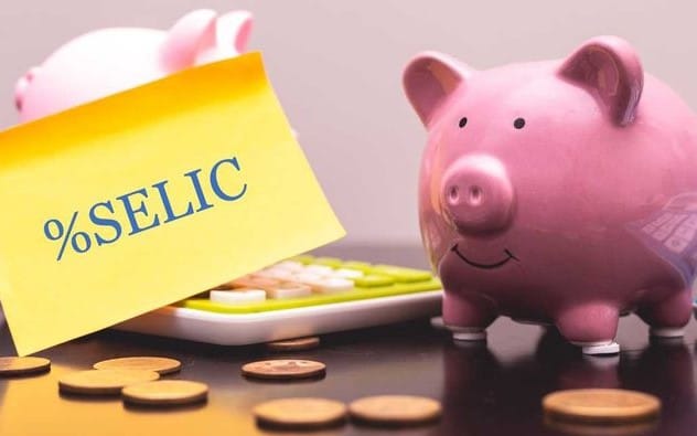 Cofrinho rosa ao lado de uma calculadora e um papel amarelo com a palavra “%Selic”, simbolizando o rendimento do Tesouro Selic como opção segura para investir a reserva de emergência quanto guardar.