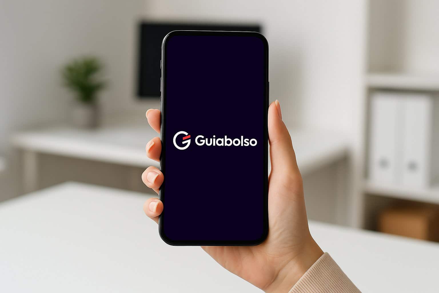 Mão feminina segurando um celular exibindo a tela com o logo do GuiaBolso, representando o uso de aplicativos para organizar finanças e gerenciar o controle financeiro pessoal em um ambiente de escritório moderno.