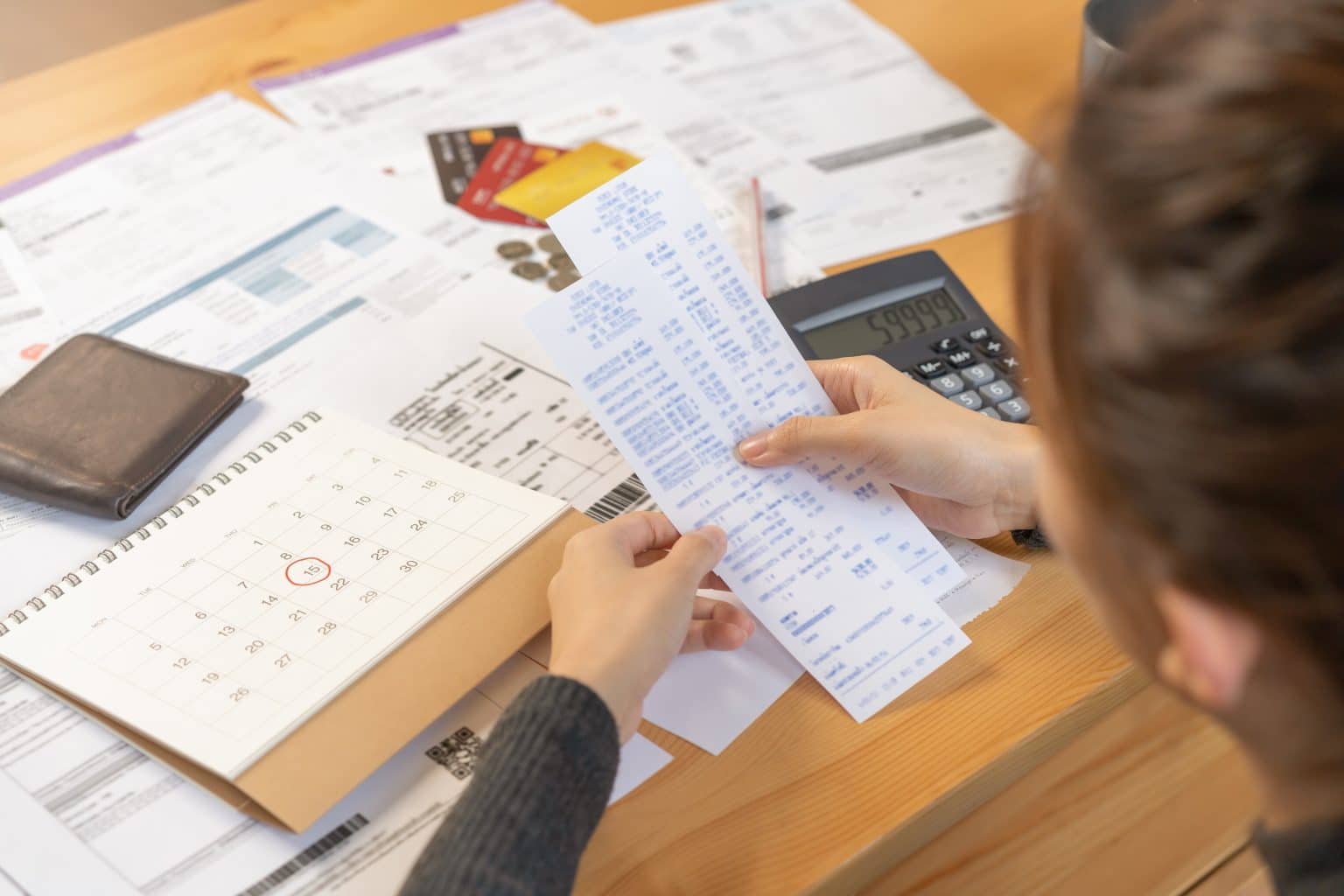 Pessoa conferindo comprovantes e calendário com data marcada, enquanto calcula como fazer um orçamento mensal.