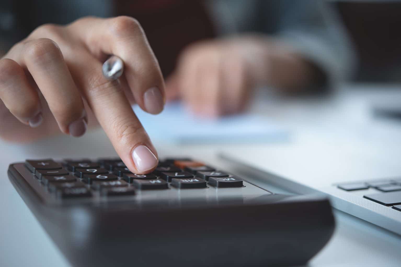 Mão feminina digitando em calculadora enquanto organiza contas e descobre como fazer um orçamento mensal.