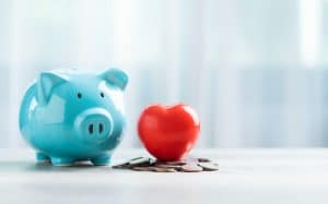 Cofrinho azul ao lado de um coração vermelho sobre moedas, simbolizando organização financeira e métodos para sair do vermelho.