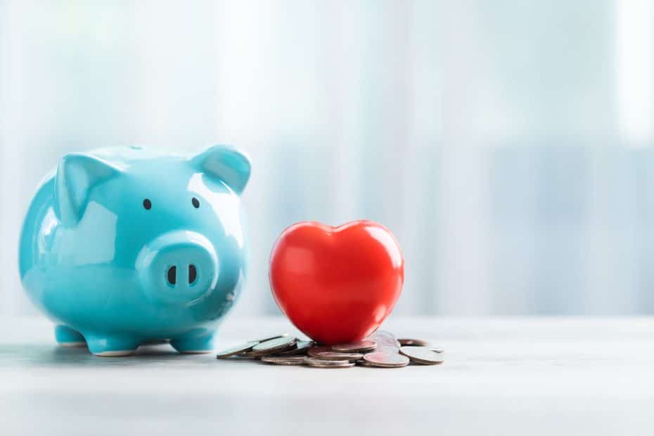 Cofrinho azul ao lado de um coração vermelho sobre moedas, simbolizando organização financeira e métodos para sair do vermelho.