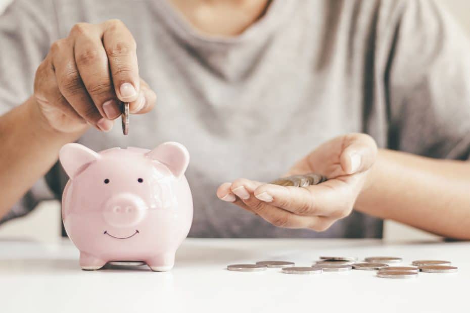 Pessoa colocando moedas em um cofrinho rosa, ilustrando dicas práticas de como guardar dinheiro ganhando pouco no dia a dia.
