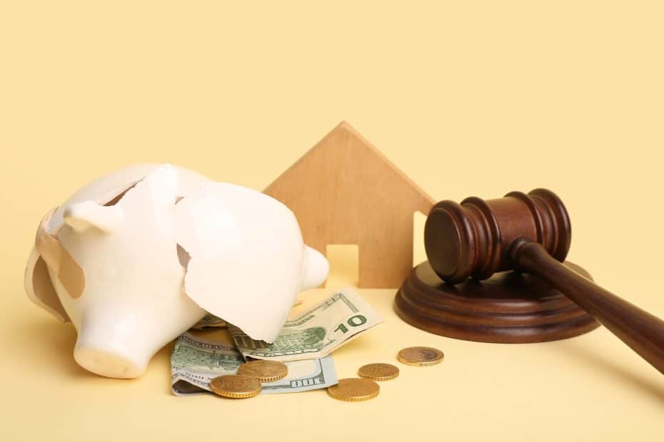 Cofrinho quebrado com dinheiro ao lado de martelo de juiz e miniatura de casa, simbolizando tarifa bancária e como evitar cobranças desnecessárias.