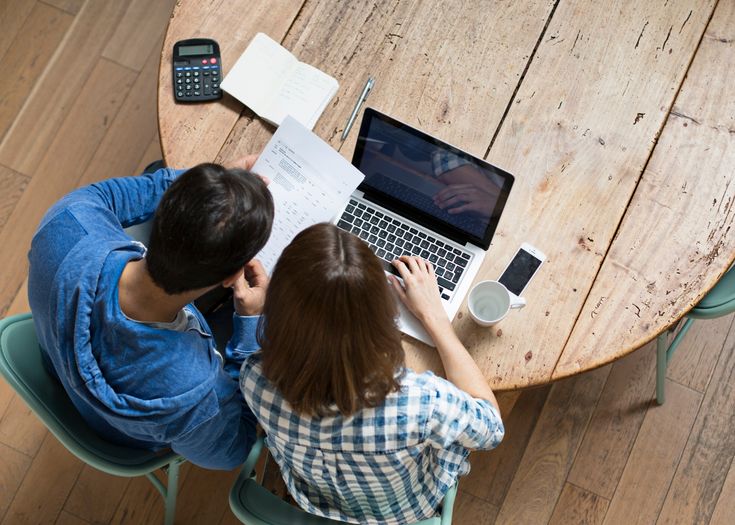 Casal analisando contas e usando notebook e calculadora para pesquisar como negociar dívidas bancárias e organizar as finanças em casa.