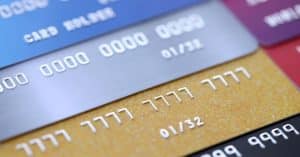 Cartão de crédito atrapalha ou ajuda o orçamento? Imagem mostra vários cartões de crédito sobrepostos em close, destacando números e validade, representando o uso frequente e o impacto no controle financeiro.